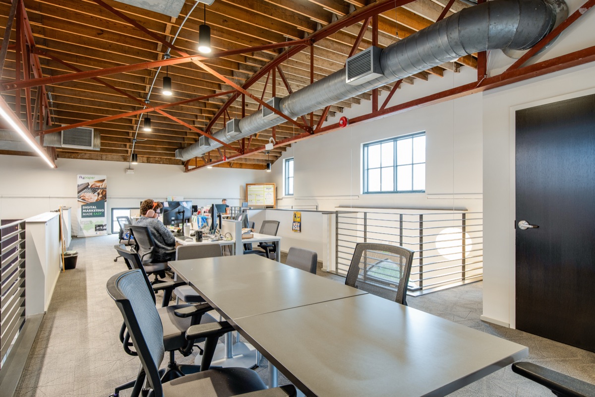 Desks along the mezzanine beneath the red steel trusses and the original wood ceiling, overlooking the main level.